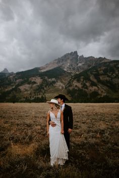 a bride and groom standing in the middle of a field with mountains in the background