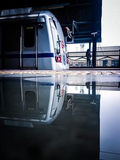 a silver train parked next to a loading platform with its reflection in the wet ground