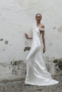 a woman in a white dress standing next to a wall