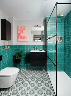 a bathroom with blue tiles and green walls, including a white toilet next to a black cabinet