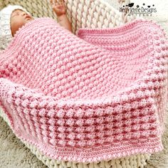 a baby is laying in a crocheted pink and white blanket on the floor