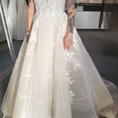 a woman standing in front of a mirror wearing a wedding dress with white flowers on it