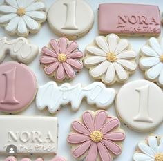 decorated cookies with flowers and numbers are displayed on a white tablecloth, including one for the first birthday