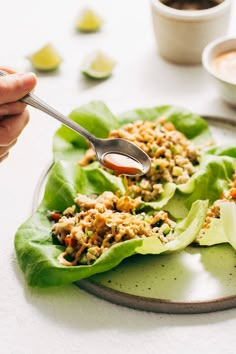 a person holding a spoon over some lettuce leaves on a plate with dipping sauce