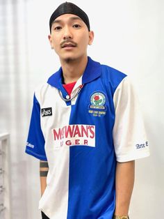 a man in a blue and white shirt standing next to a wall with his hand on his hip