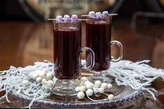 two glasses filled with purple liquid sitting on top of a glass plate next to white balls