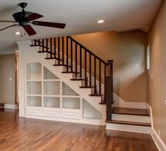 a living room with hard wood floors and white bookcases under a ceiling fan