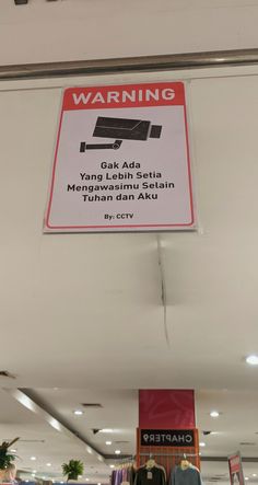 a sign that is hanging from the ceiling in a store with clothes on display behind it