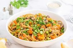 a white bowl filled with noodles and vegetables on top of a table next to silverware