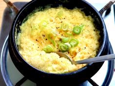 a bowl filled with mashed potatoes and green onions on top of a stovetop