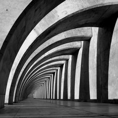 black and white photograph of an arched walkway with concrete columns on either side, leading into the distance