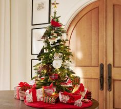 a christmas tree with presents under it on a table in front of a wooden door