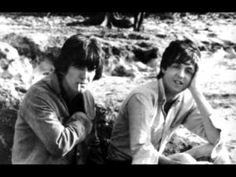 two young men sitting next to each other on top of a sandy beach covered in grass