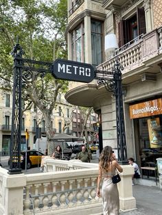 a woman walking down the street in front of a metro sign on a city street