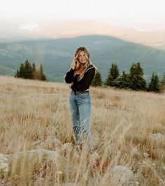 a woman standing on top of a grass covered field with mountains in the back ground