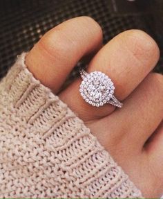 a woman's hand with a diamond ring on top of her finger, wearing a sweater