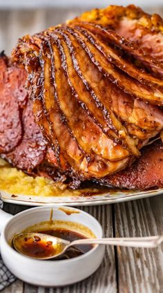 a ham is sitting on top of mashed potatoes next to a bowl of sauce