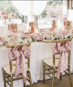 the table is set with pink flowers and gold chairs for guests to sit down at