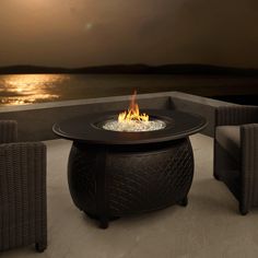 an outdoor fire pit sitting on top of a patio next to some wicker chairs