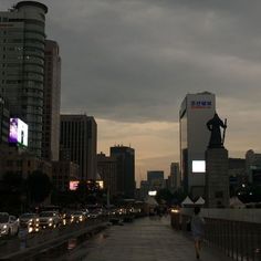 a person walking down a sidewalk in front of some tall buildings with lights on them