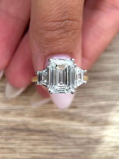 a woman's hand holding an emerald and diamond ring