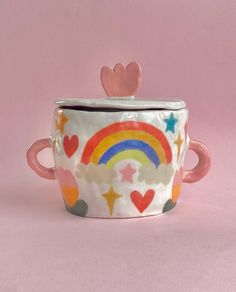 a coffee cup with hearts and rainbows painted on the inside is sitting in front of a pink background