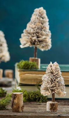 three fake trees sitting next to each other on top of a wooden table with moss growing out of them