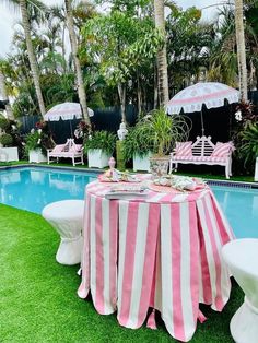 a pink and white striped table cloth next to a pool with umbrellas over it