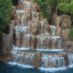 a large waterfall in the middle of a pool surrounded by rocks and water features several waterfalls