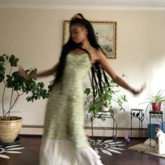 a woman with long hair dancing in a living room next to a potted plant