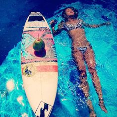 a woman is floating in the water next to a surfboard