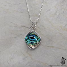 "A square piece of green-blue abalone shell is held tight by sterling silver spirals in this wire wrapped pendant. The shimmery abalone (also called paua) shell is a beautiful sea-foam green with brown concentric patterns like rippling waves. It has flashes of blue and gold and even a subtle violet that skitter across the iridescent surface as it moves on the wearer. The bright silver spirals balance the brown lines and emphasize the watery feel of the colors and movement of light. It's by no me Abalone Necklace, Paua Shell, Silver Chain Style, Sterling Silver Wire Wrap, Gold Paper, Wire Wrapped Necklace, Shell Necklace, Metallic Blue, Resin Pendant