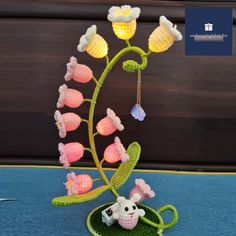 a crocheted plant with flowers and a small animal on it's head