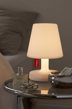 a table with a lamp on top of it next to a bottle of perfume and a pillow