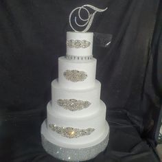 a three tiered wedding cake with crystals on the top and bottom, is displayed in front of a black backdrop