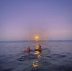 two people are swimming in the ocean at sunset or dawn with their backs turned to the camera