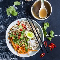 a white plate topped with noodles and veggies next to two bowls of soup