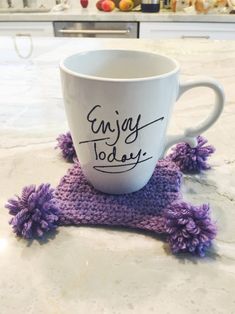 a coffee cup sitting on top of a counter next to a purple pom - pom