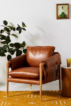 a brown leather chair sitting next to a potted plant on top of a yellow rug