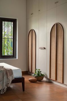 a bedroom with two arched windows and a bed in front of the window, next to a potted plant