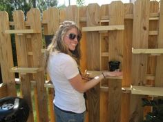 a woman standing in front of a wooden fence holding a potted plant and smiling