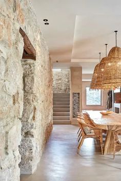 a dining room table and chairs in front of a stone wall with lights hanging from it