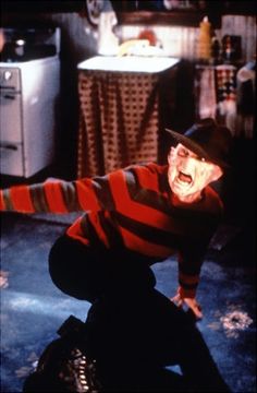 a man in striped shirt and hat with arms outstretched on floor next to kitchen area