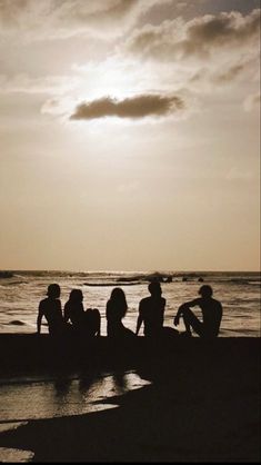 four people sitting on the beach watching the sun go down over the ocean with clouds in the sky