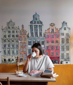 a woman sitting at a table with a book and cup in front of her face