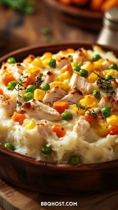 a wooden bowl filled with mashed potatoes covered in chicken and vegtables