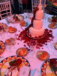 a wedding cake on top of a table surrounded by plates and glasses with rose petals