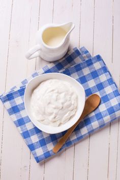 a bowl of yogurt on a blue and white checkered napkin next to a spoon