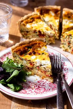 a piece of quiche on a plate next to a fork and glass of water