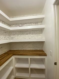 an empty walk in closet with white shelving and wooden shelves on the wall next to it